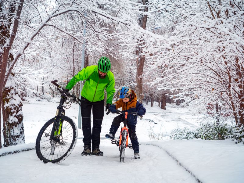 En man hjälper ett barn på en cykel i ett vintrigt landskap