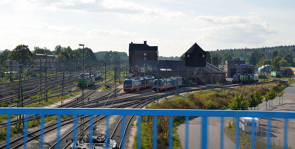 Viaduktens blå staket i förgrunden. Bakom syns järnvägsspåren och tågset på rangerbangården.
